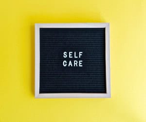 A board that reads, "self care," which is an important part of a creative routine for professionals.