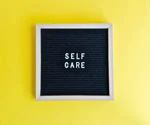 A board that reads, "self care," which is an important part of a creative routine for professionals.